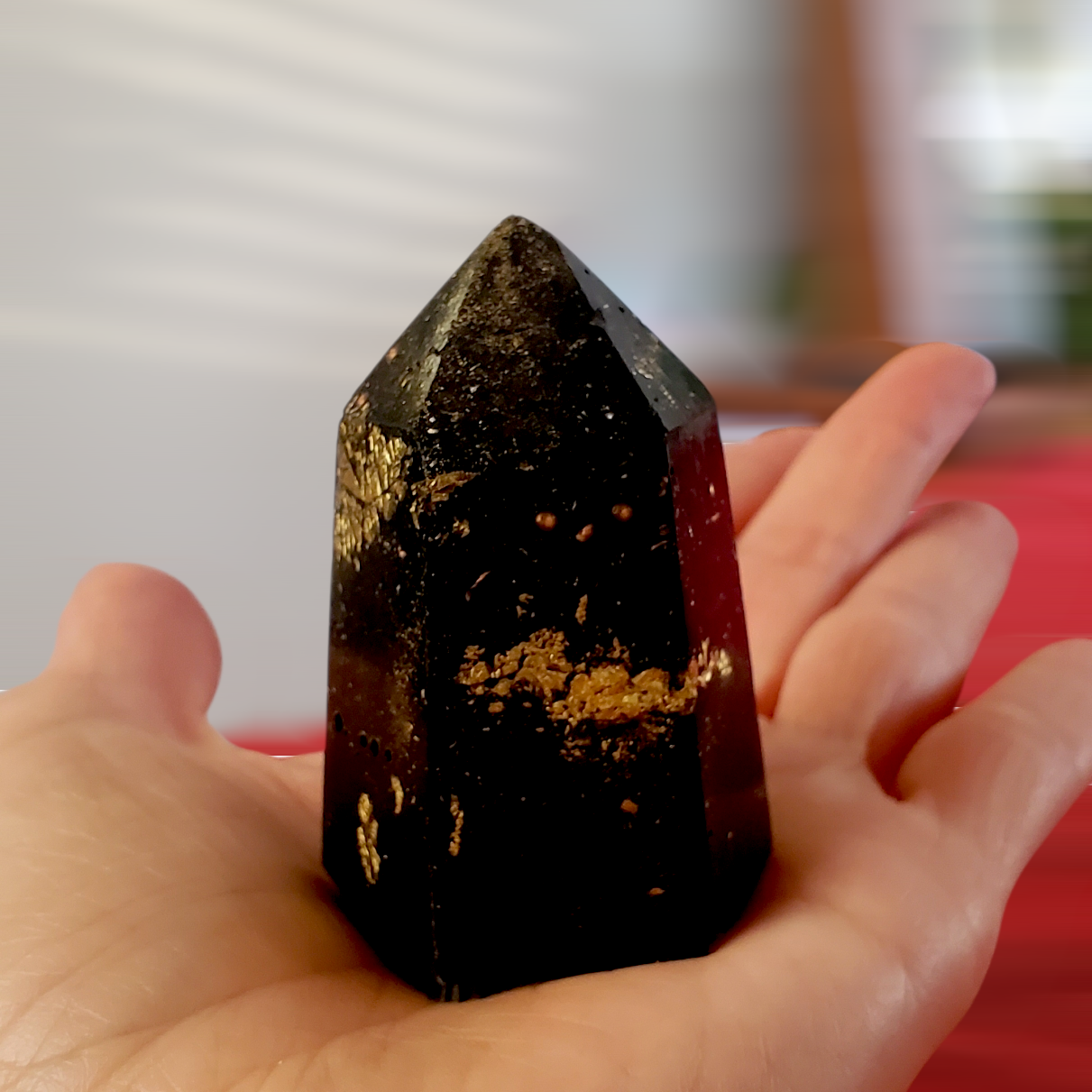 Hand holding an orgonite l with gold flecks against a blurred background