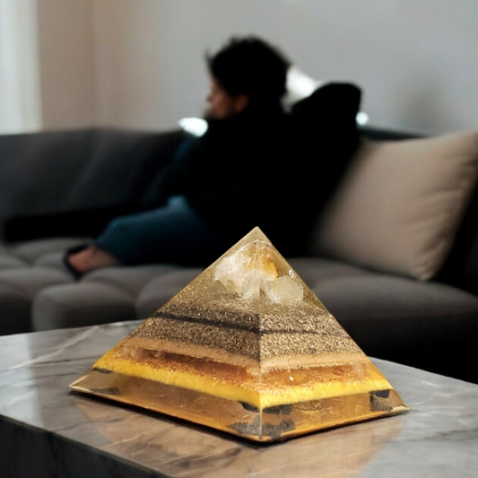 Pyramid-shaped orgonite on a marble surface with a blurred background of a person sitting on a couch.