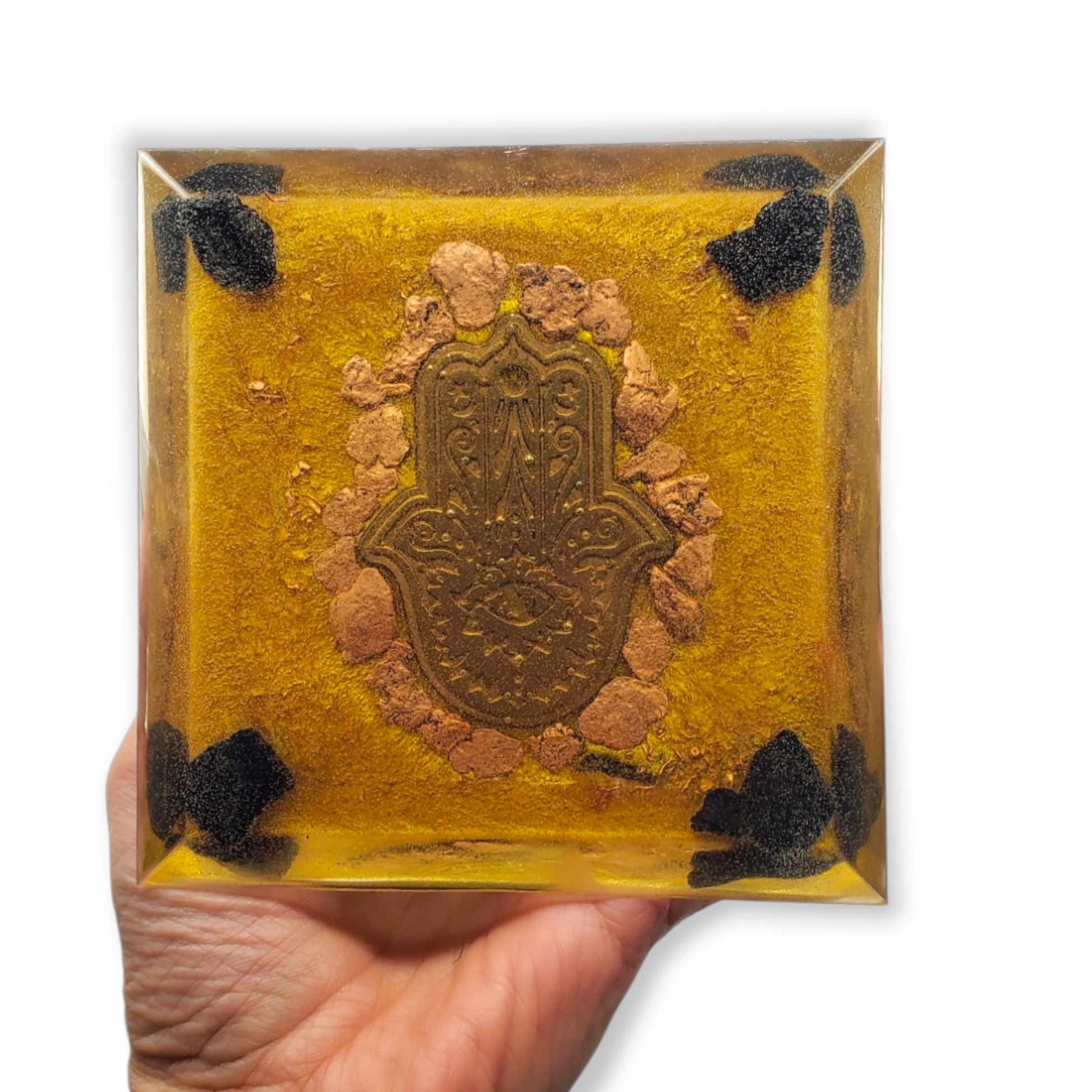 Decorative square orgonite with Hamsa design held by a hand on a white background